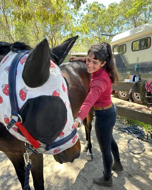 Ostéopathe équine caressant un cheval équipé d'un masque anti-mouches avant sa séance